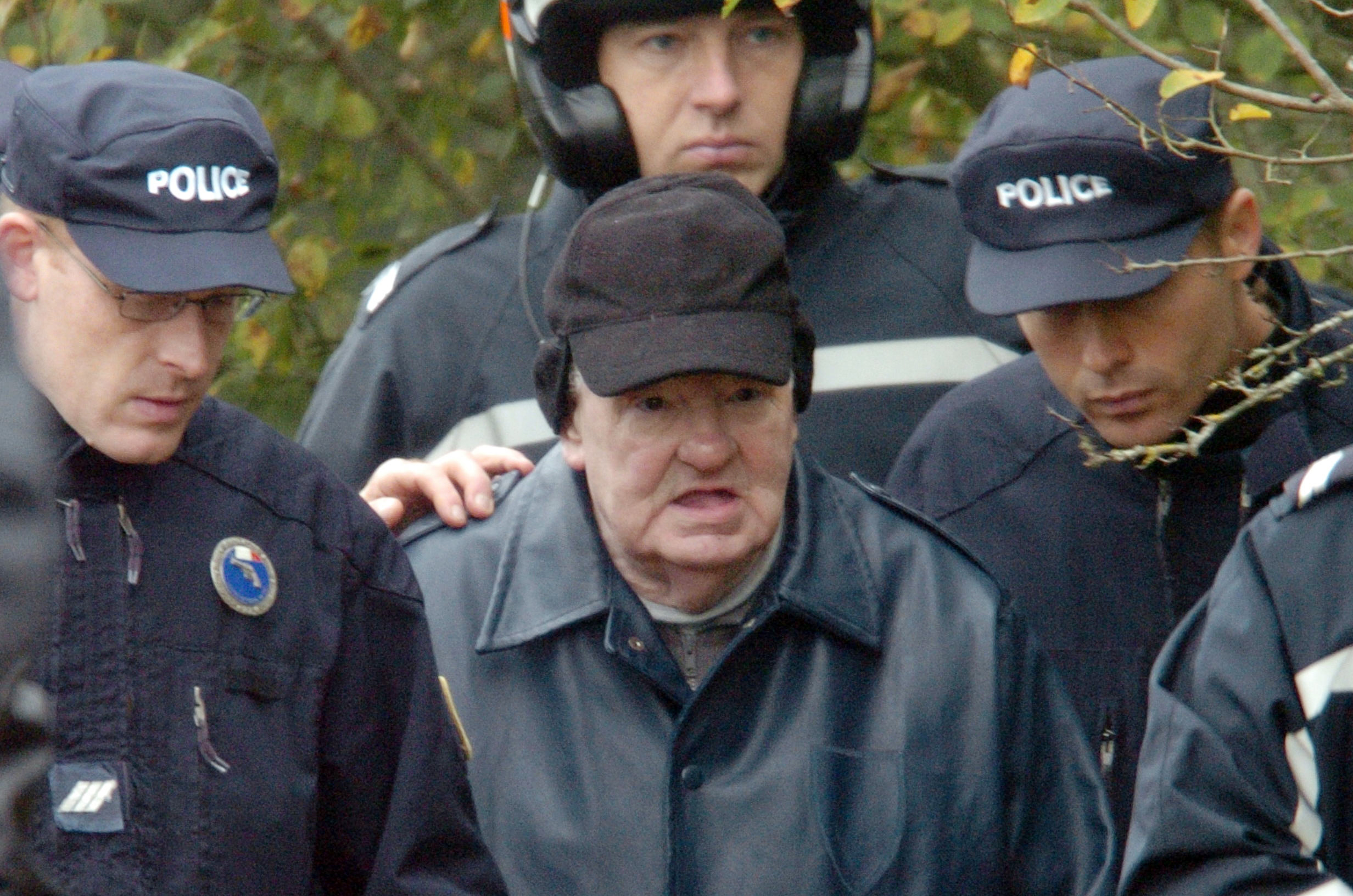 Emile Louis escorté par la police le 10 novembre 2004 à Rouvray lors de son procès à l'endroit où les cadavres de deux victimes -Madeleine Dejust et Jacqueline Weis- ont été découverts en 2001.