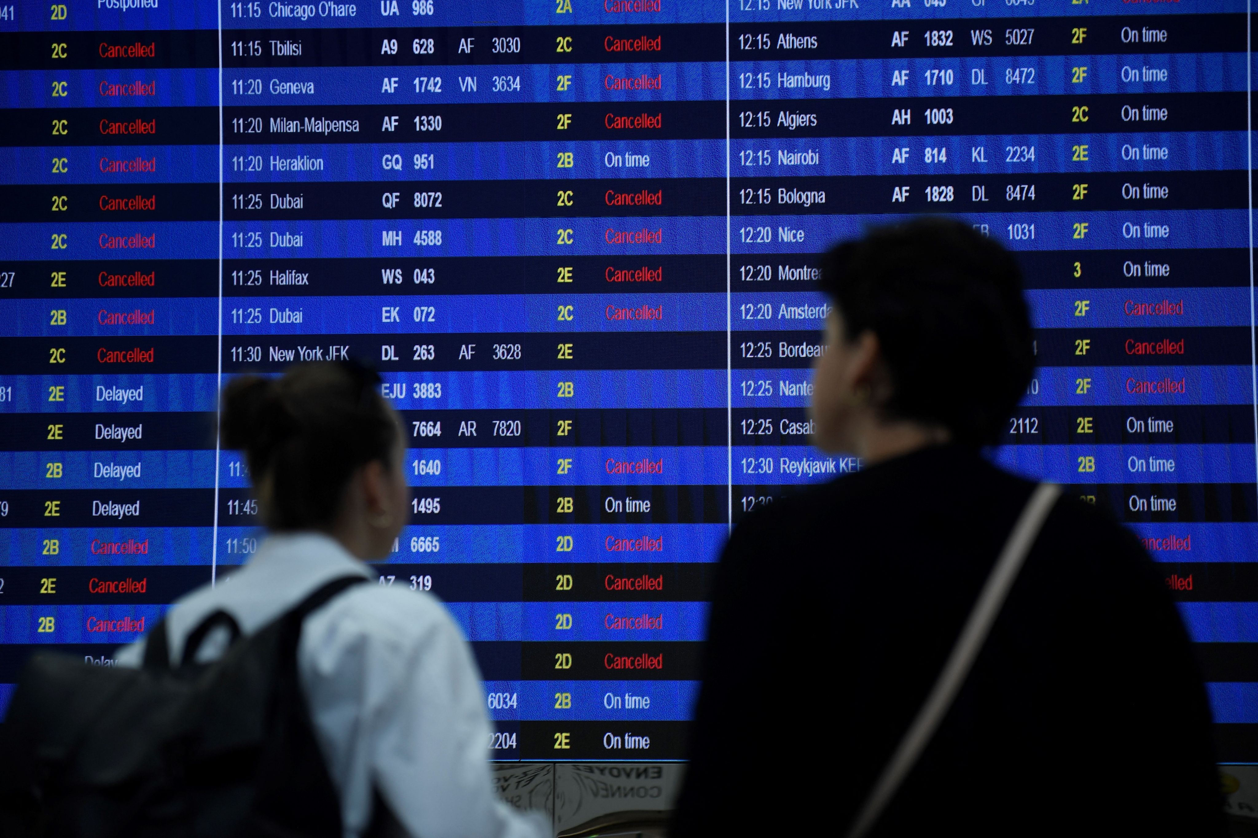 Des voyageurs regardent le panneau d'information sur les départs du terminal 2 de l'aéroport Roissy-Charles de Gaulle, dans la banlieue nord-est de Paris