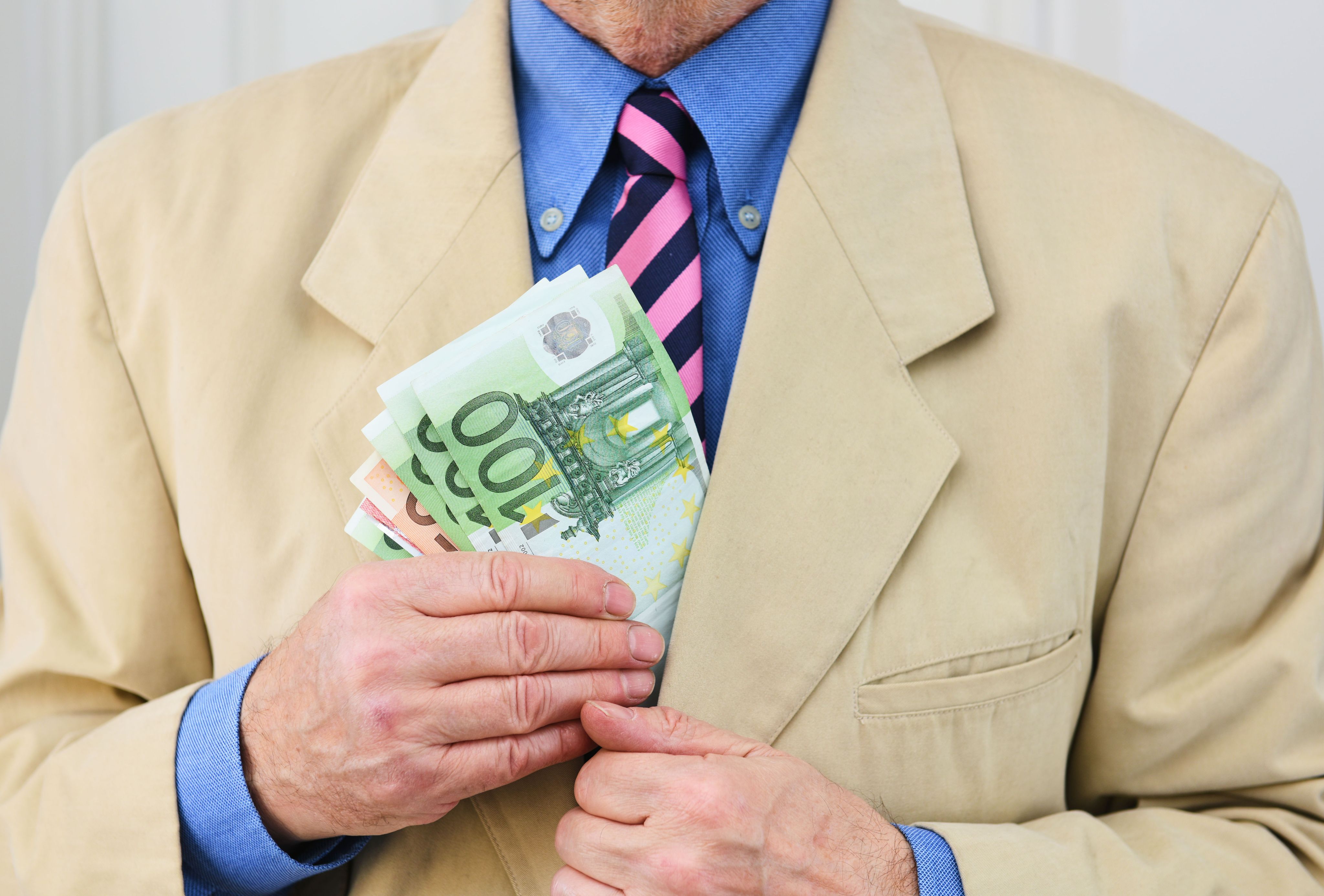 Un riche homme d’affaires prend ou glisse des liasses de billets dans sa poche, symbole contemporain des fortunes et des débats sur la taxation des ultra-riches