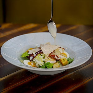 A bowl of caesar salad with a spoon drizzling the dressing over it.