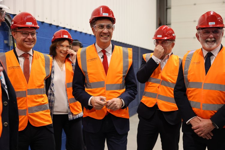 Ed Miliband, Michael Shanks, and Jürgen Maier wear red hard hats, safety glasses, and orange high-visibility vests at the Floating Wind Innovation Centre.