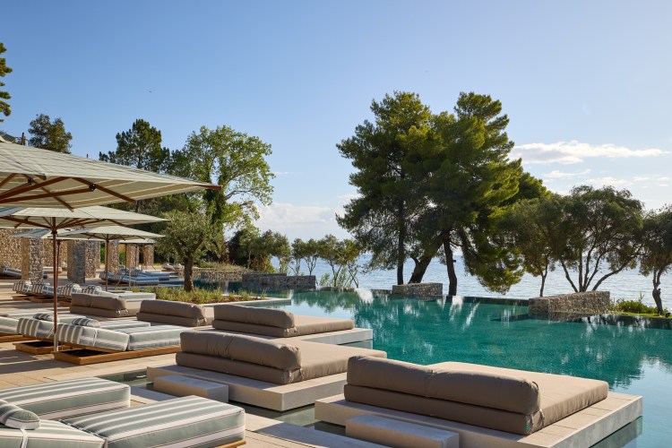 Outdoor seating area with umbrellas and daybeds by an infinity pool overlooking the sea.