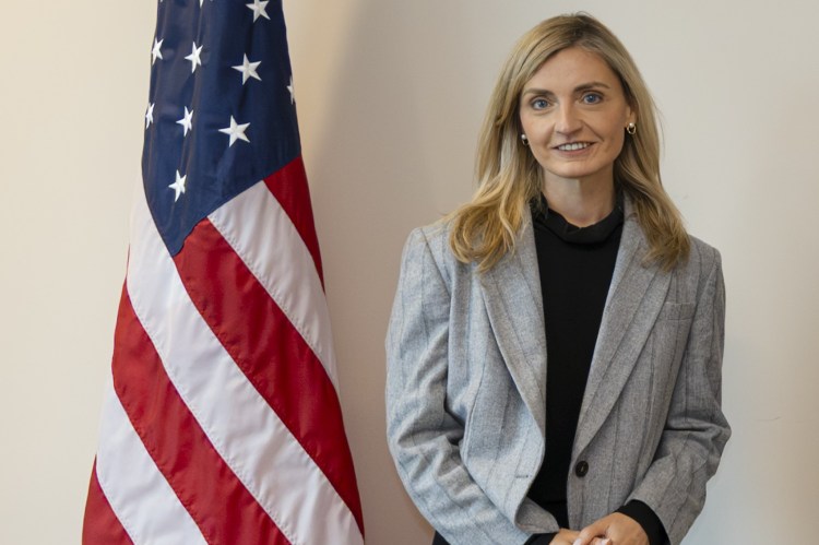 Under Secretary of State Sarah B. Rogers stands next to a US flag.