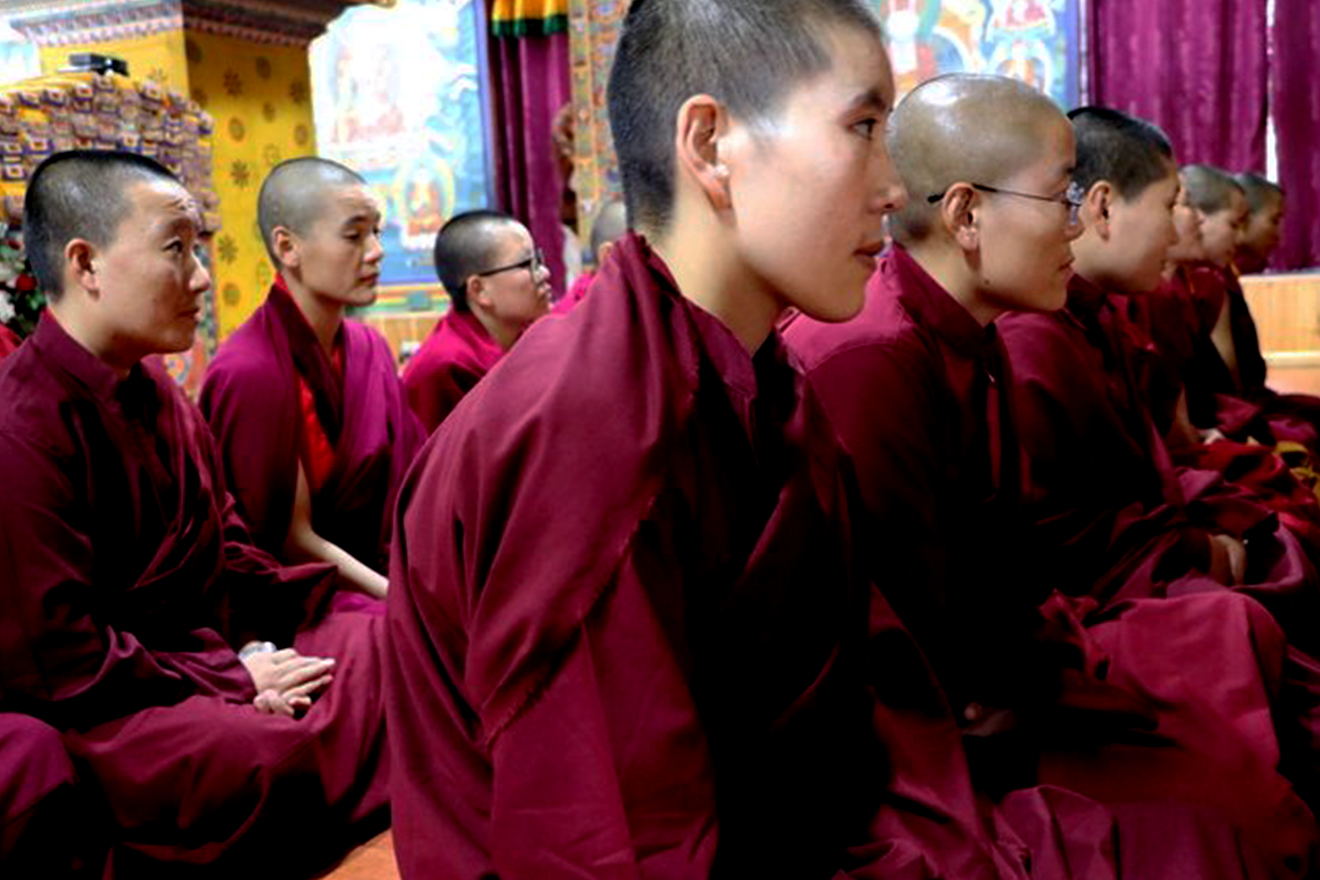 Nuns and monks, instructors in life-skills education, Bhutan. Nuns and monks, with shaved heads and dressed in crimson robes, sit in organized rows as they look ahead in unison.