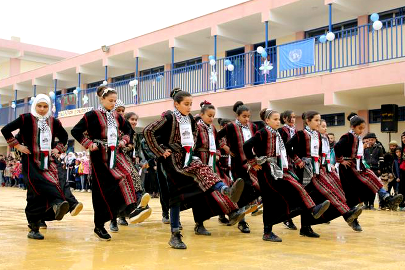Palestine refugee students perform a folklore dance in celebration of the inauguration of their new school in Dera'a refugee camp, Syria. Palestinian girls, donning traditional garments, dance dabkeh in a school yard.