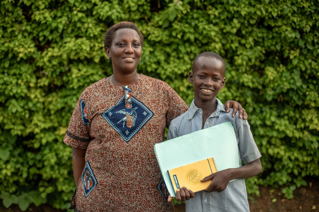 Yvonne stands next to Eric, who proudly holds his newest school books wearing his school uniform. Yvonne stands next to Eric, who proudly holds his newest school books wearing his school uniform.