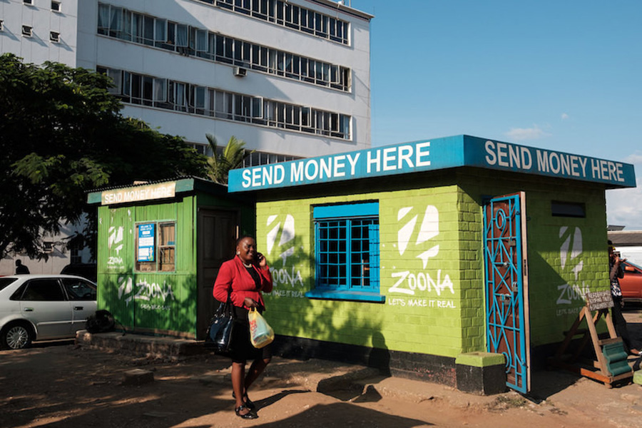 Remittances often hold up in response to adverse shocks in recipient countries. Photo: World Bank / IFC Woman walking by a store with a sign that reads “Send money here”.