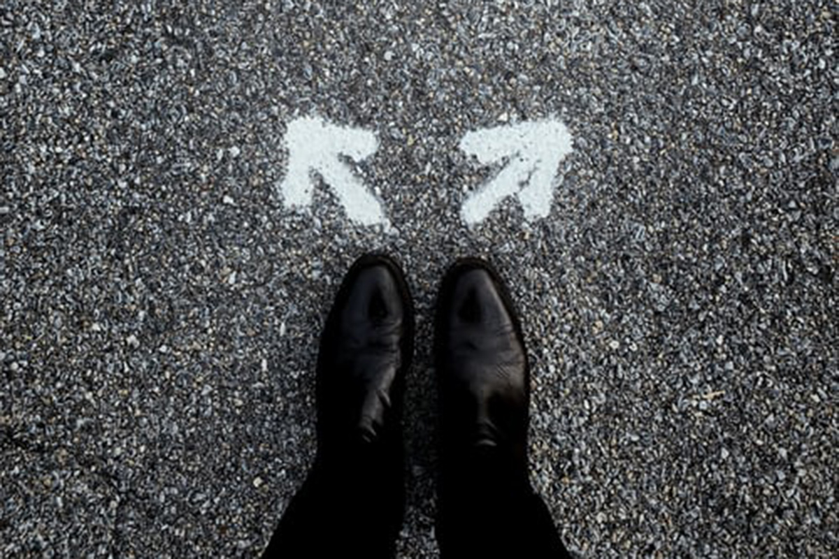 Uncertainty in systemic economies matters for uncertainty around the world. Photo: Unsplash / Jon Tyson View of two feet standing in front of arrows pointing in opposite directions.