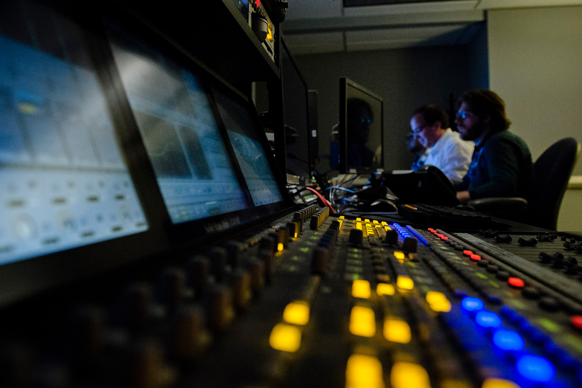 Detail of the TV control panel in the foreground with two TV technicians in the background.