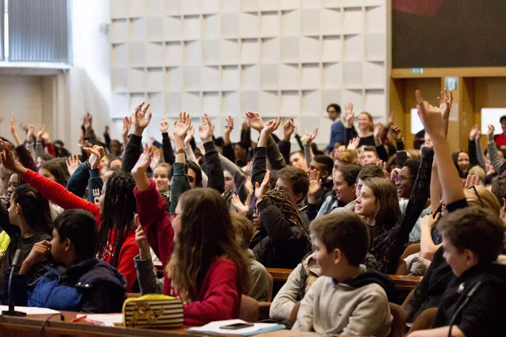 A group of students raising their hands in a big auditorium.