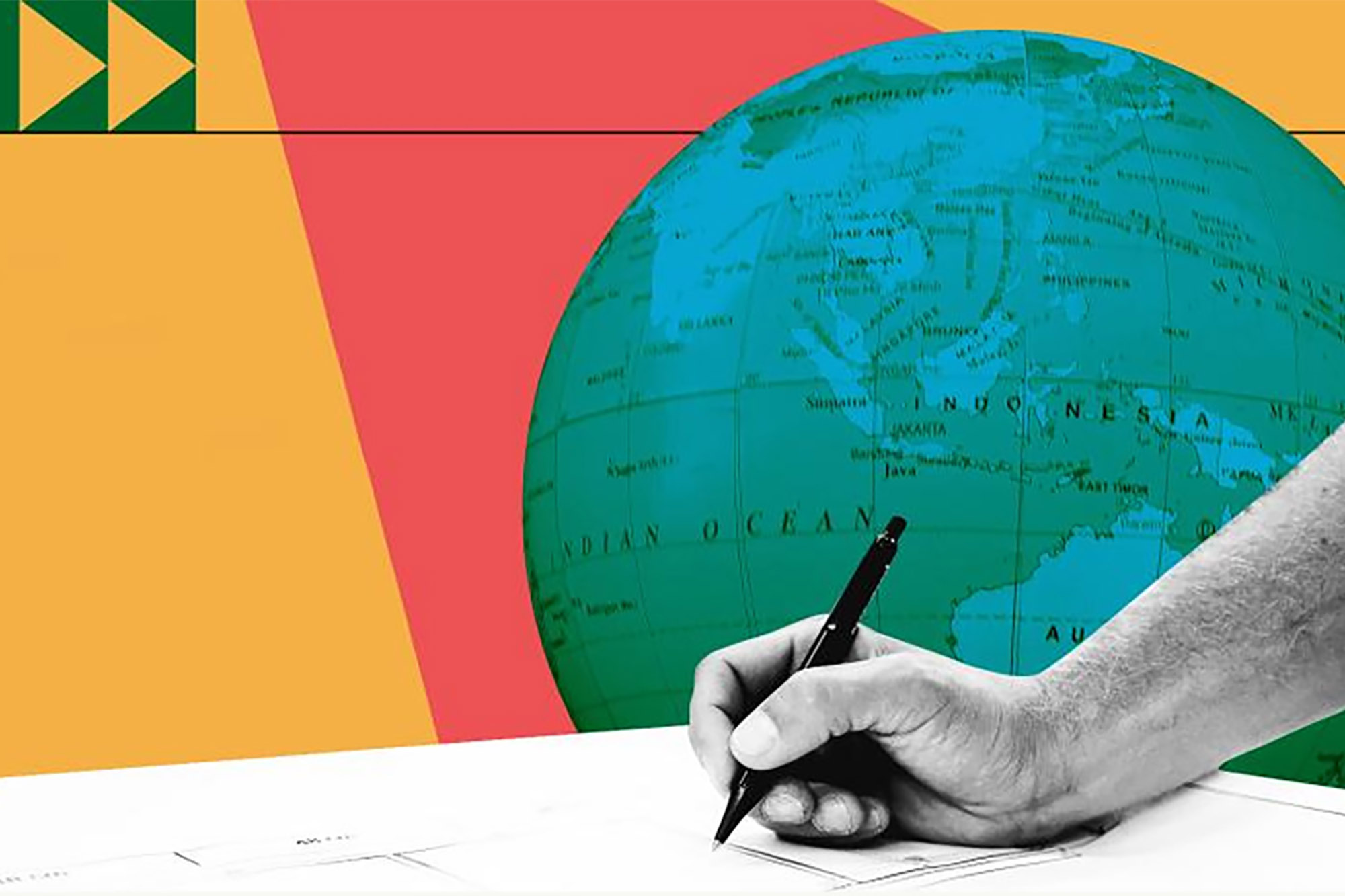 A hand holding a pen and writing on a piece of paper. Behind it is a large globe and geometric shapes in green, yellow and red.