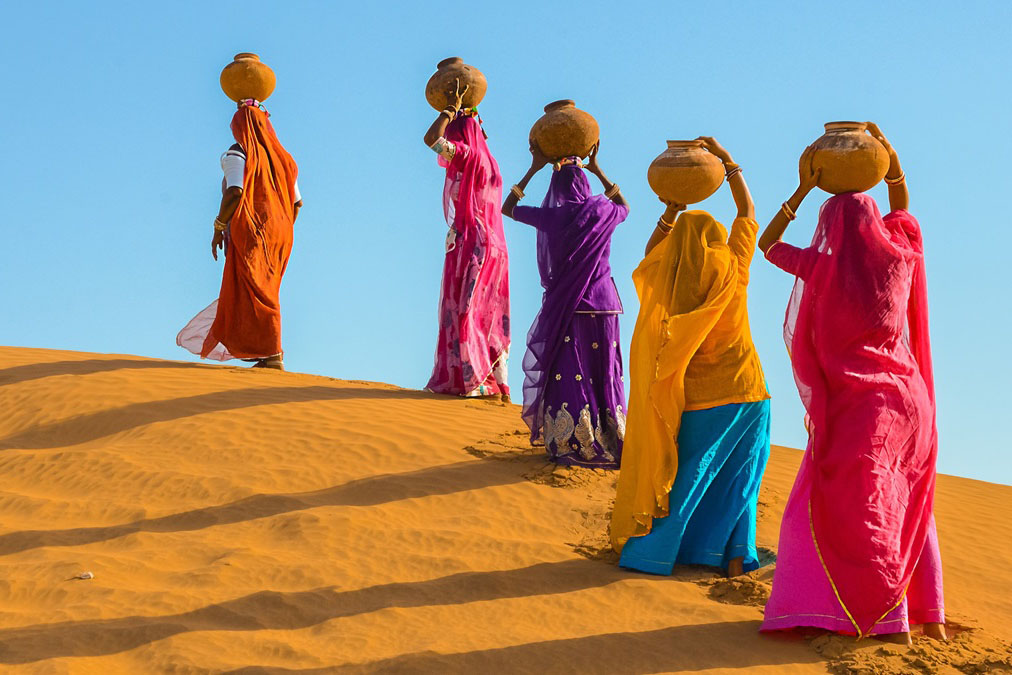 women walking on sand with jugs on their heads