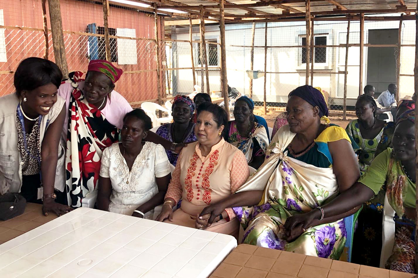 Pramila Patten sitting with many women holding their hands as they tell their harrowing stories