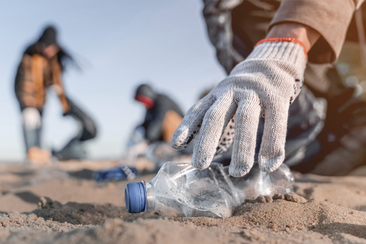 Close-up of a hand picking up a plastic bottle on the beach
