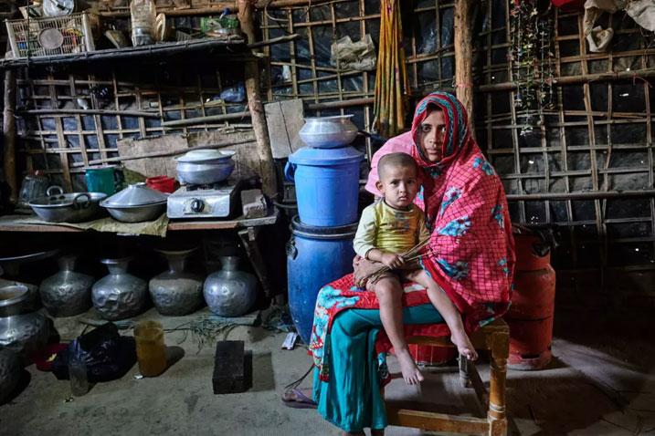 mother sits with a toddler on her lap in a dust-floor, neat and tidy kitchen