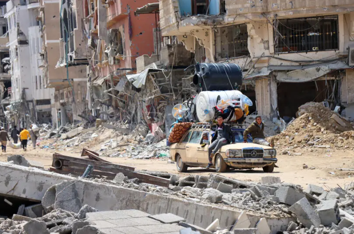 ©OCHA/Themba Linden. a city in utternm ruins and a car is trying to escape with people and items atop it