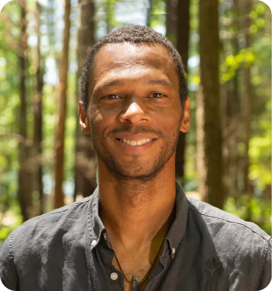 Smiling man with short hair, wearing a dark shirt, outdoors in a forest.